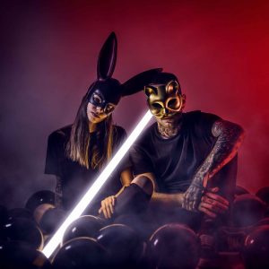 Dos artistas con máscaras y barras luminosas frente al público