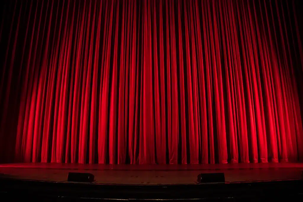 Telón rojo de un teatro iluminado; imagen ilustrativa de espectáculo